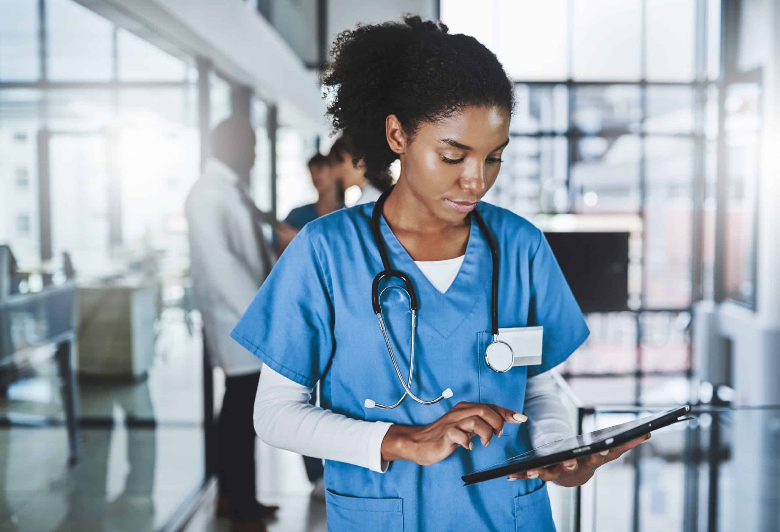 Shot of a young doctor using a digital tablet in a hospital with her colleagues in the background.