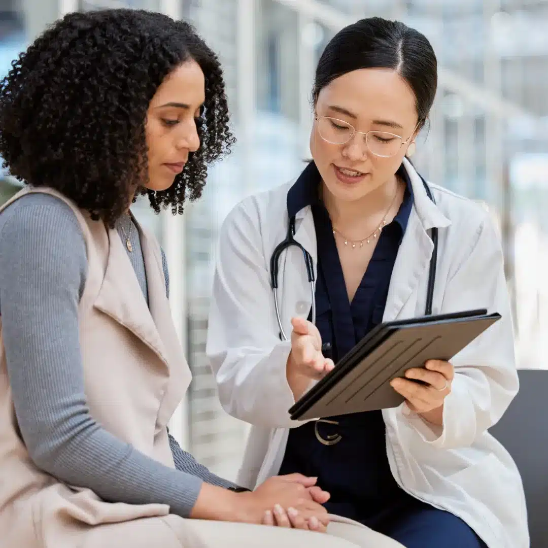 Female doctor in a white coat showing a patient information on a tablet during a clinical consultation.