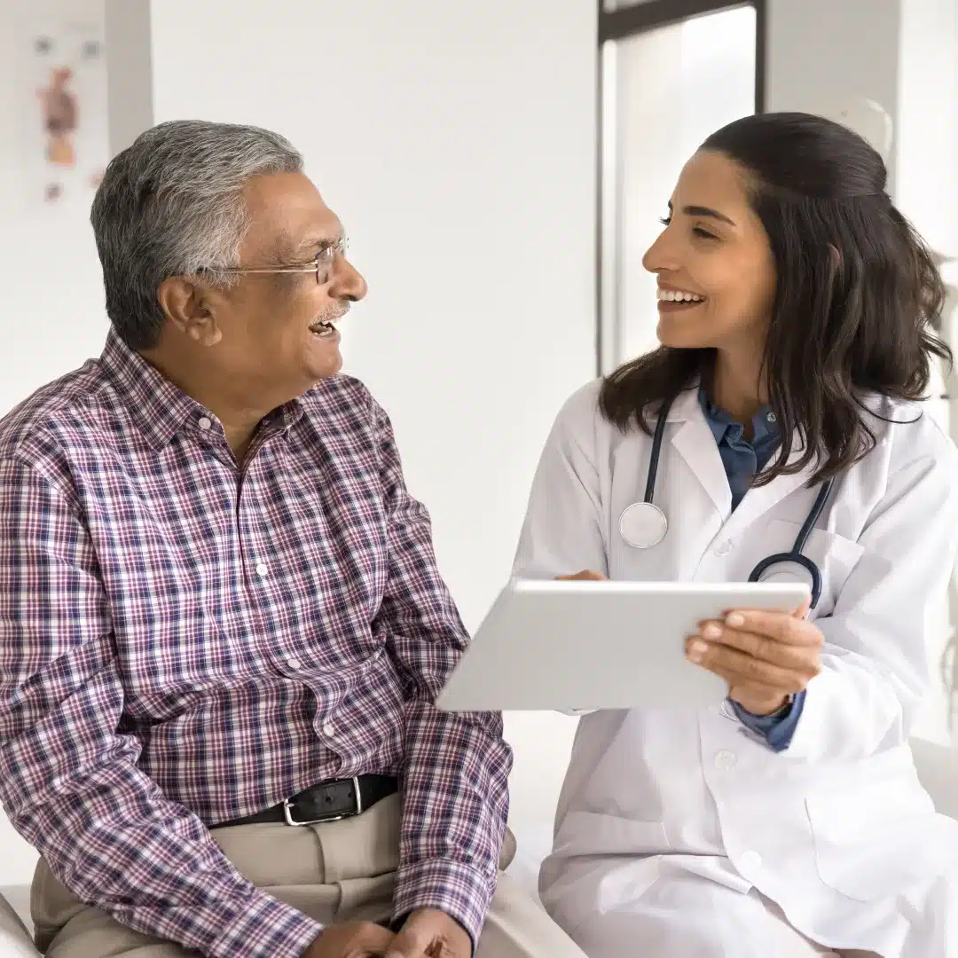 Female physician in a white coat discussing a tablet with a smiling elderly male patient in a clinic.