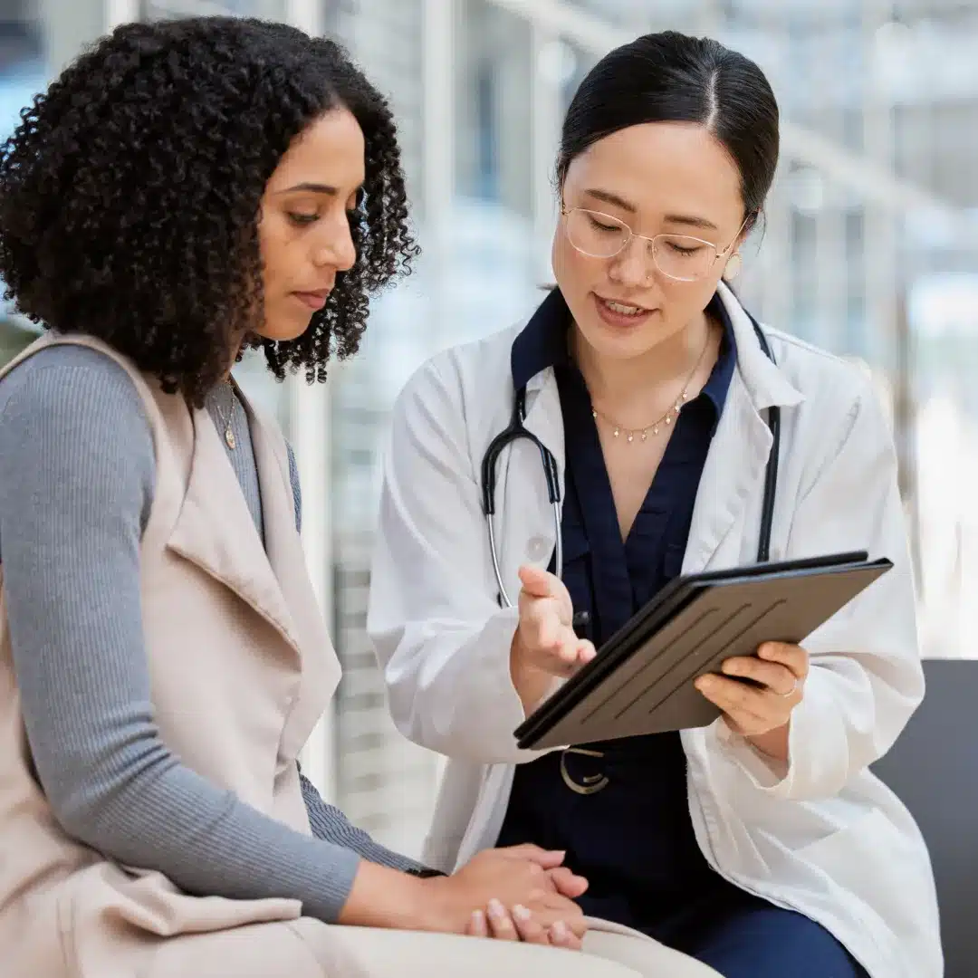 Female doctor in a white coat showing a patient information on a tablet during a clinical consultation.