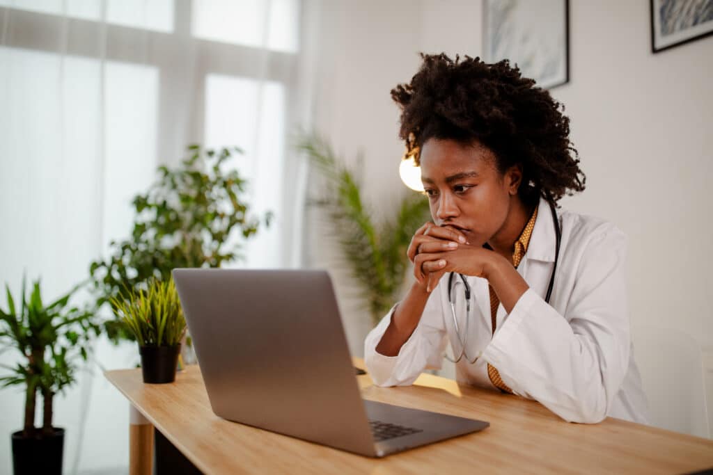 Worried black female doctor working on computer at her desk.