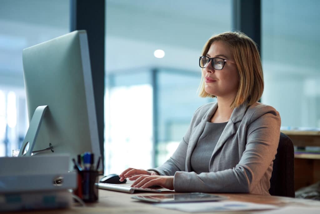 Computer, typing and business woman in office working late on project at night alone. Desktop, professional and female person writing email, report or planning, reading and overtime for deadline