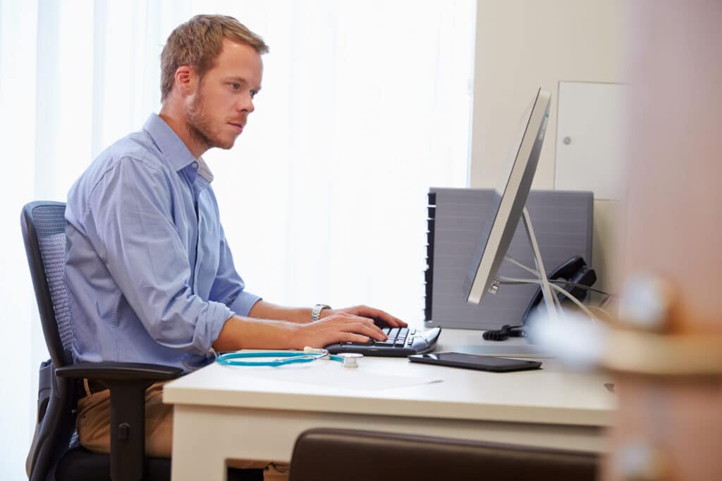 Male Doctor In Office Working At Computer