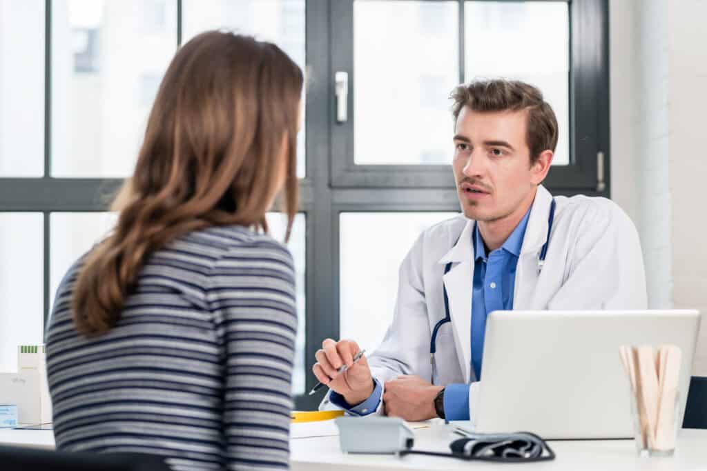 Young devoted doctor holding an X-ray while listening with attention to his female patient during a private consultation in the office