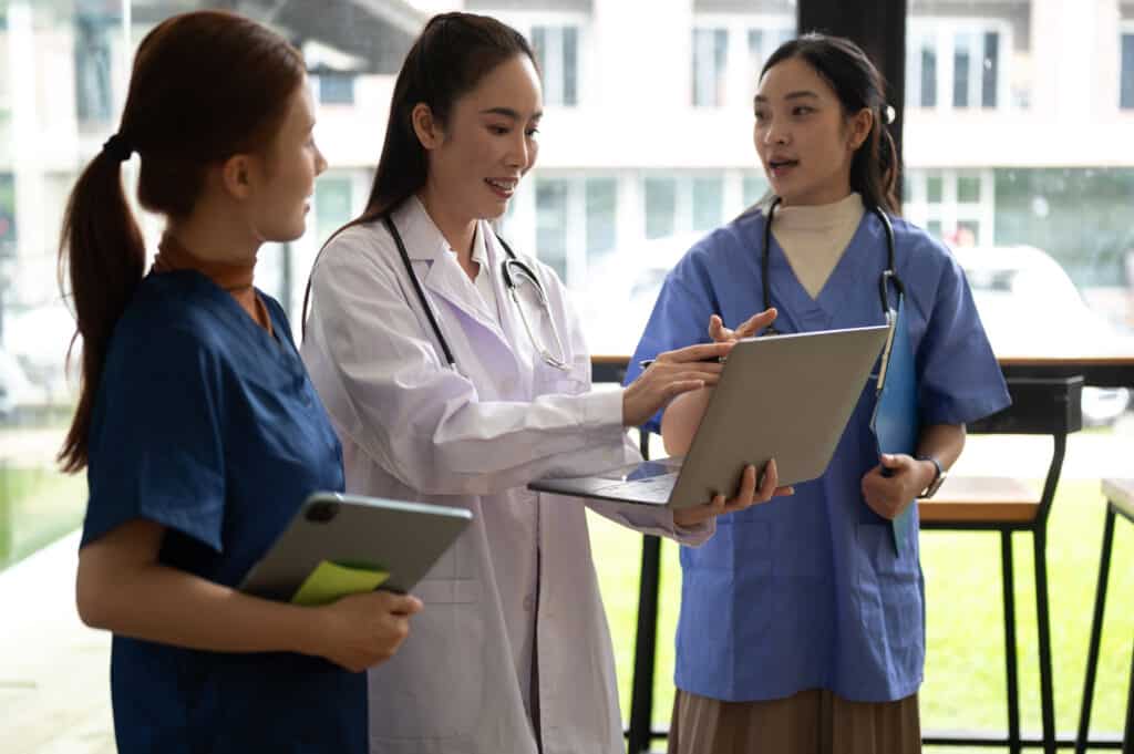 Doctors and nurses work together to review medical records and discuss patient care using digital technology in a modern healthcare setting.
