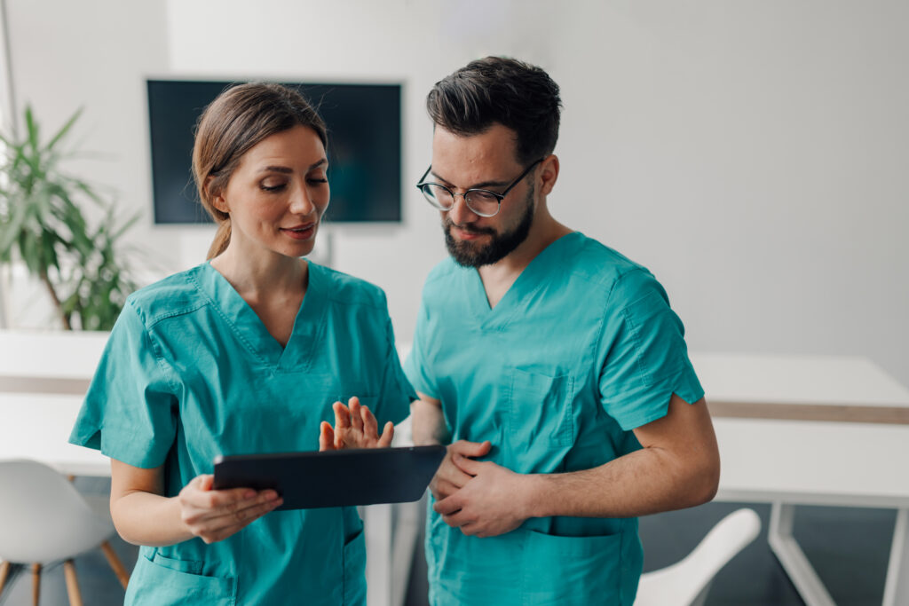 Two medical professionals are using a tablet and discussing a patient's medical history in a modern hospital room, showcasing teamwork and digital healthcare