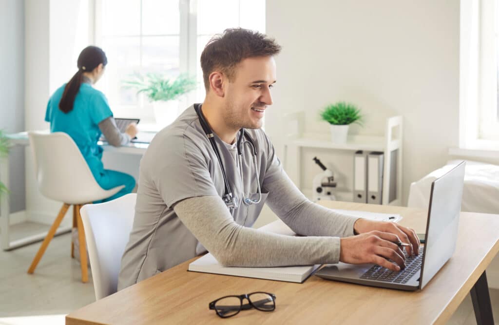 Happy man, doctor or nurse, working online with laptop, conducting research in clinic or hospital, healthcare and medical dedication in a professional environment focused on patient well-being.