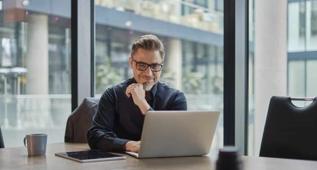 Businessman using laptop computer in office. Happy middle aged man, entrepreneur, small business owner working online.
