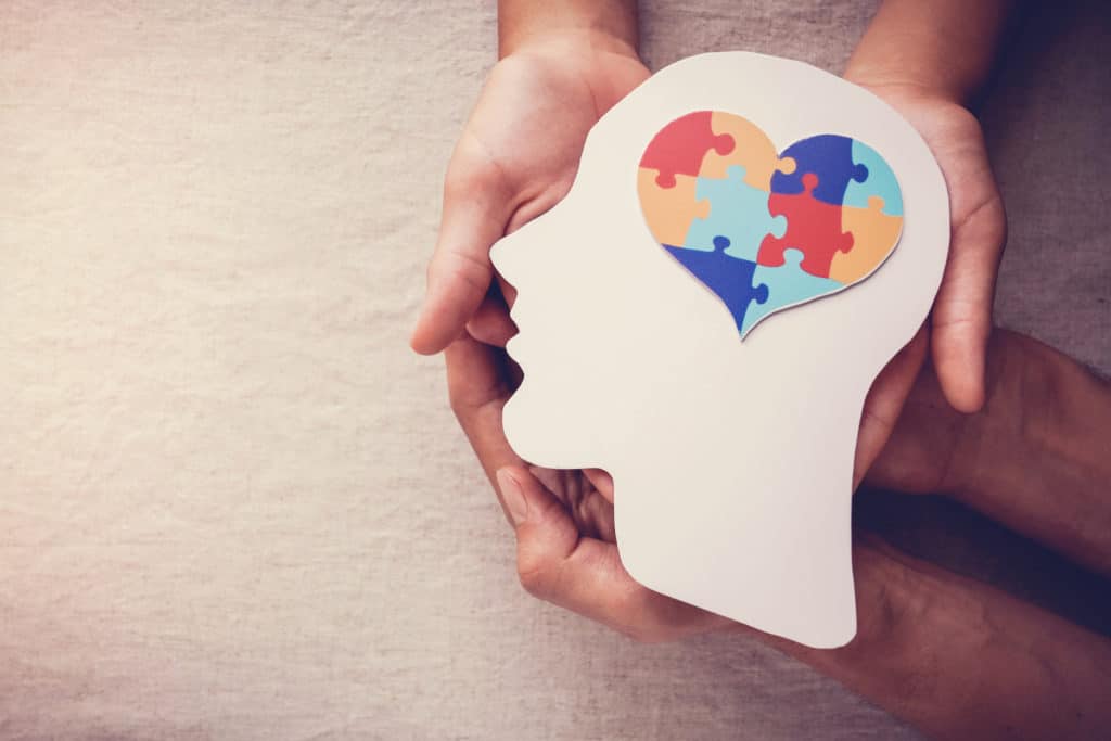 Hands holding a face shape with jigsaw puzzle heart.
