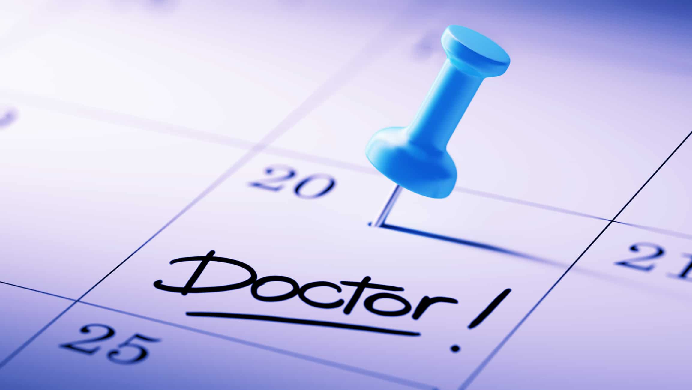 Concept image of a Calendar with a blue push pin. Closeup shot of a thumbtack attached. The words Doctor written on a white notebook to remind you an important appointment.