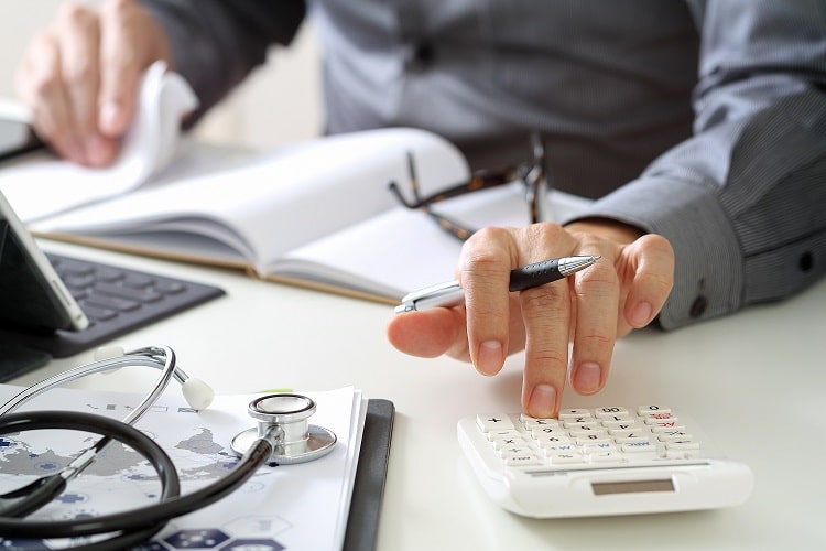 Doctor's desktop using calculator while holding a pen.