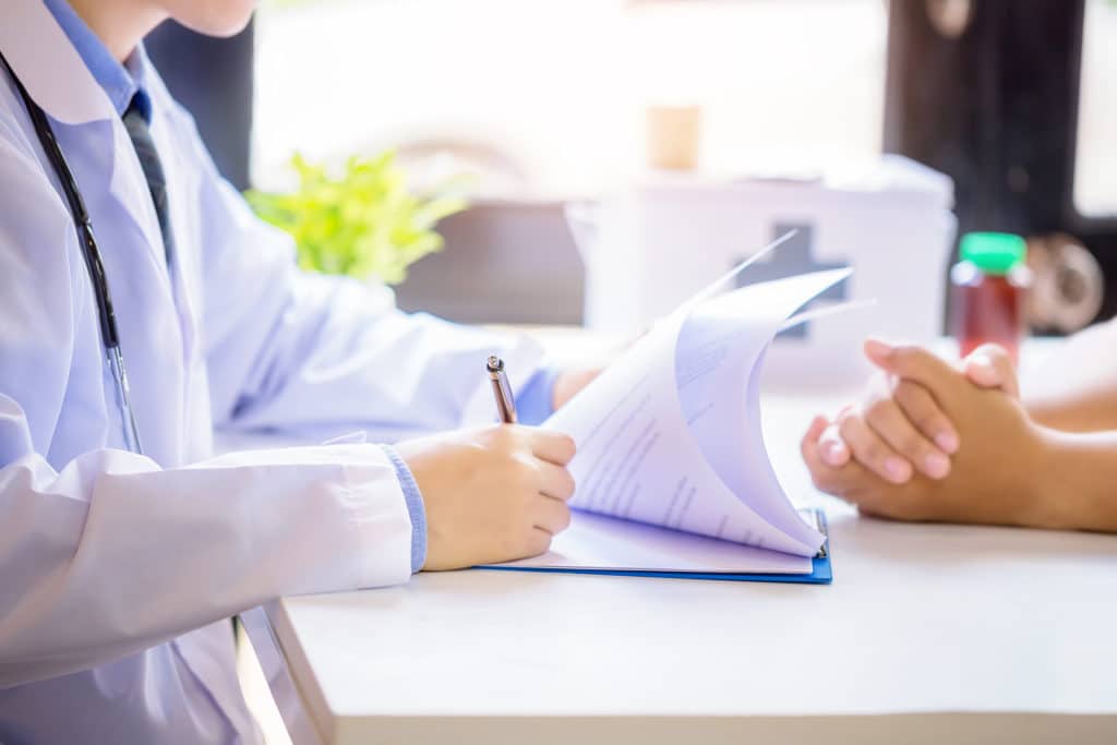 Doctor man consulting patient while filling up an application form at the desk in hospital.