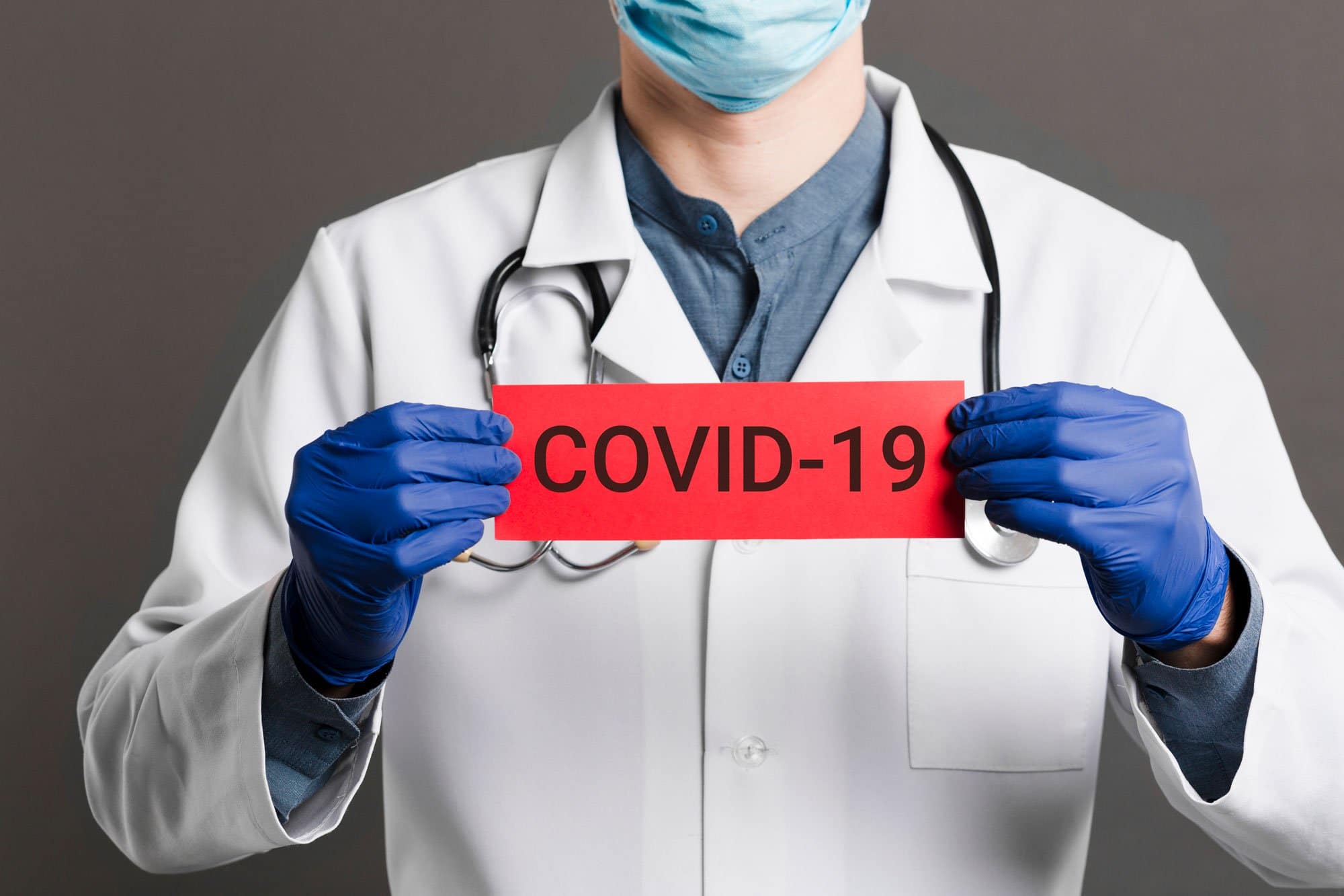 Doctor wearing mask and gloves holding a COVID-19 sign