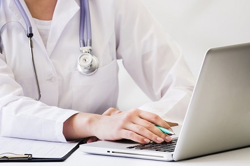 Female doctor holding a pen while using a laptop at her desk